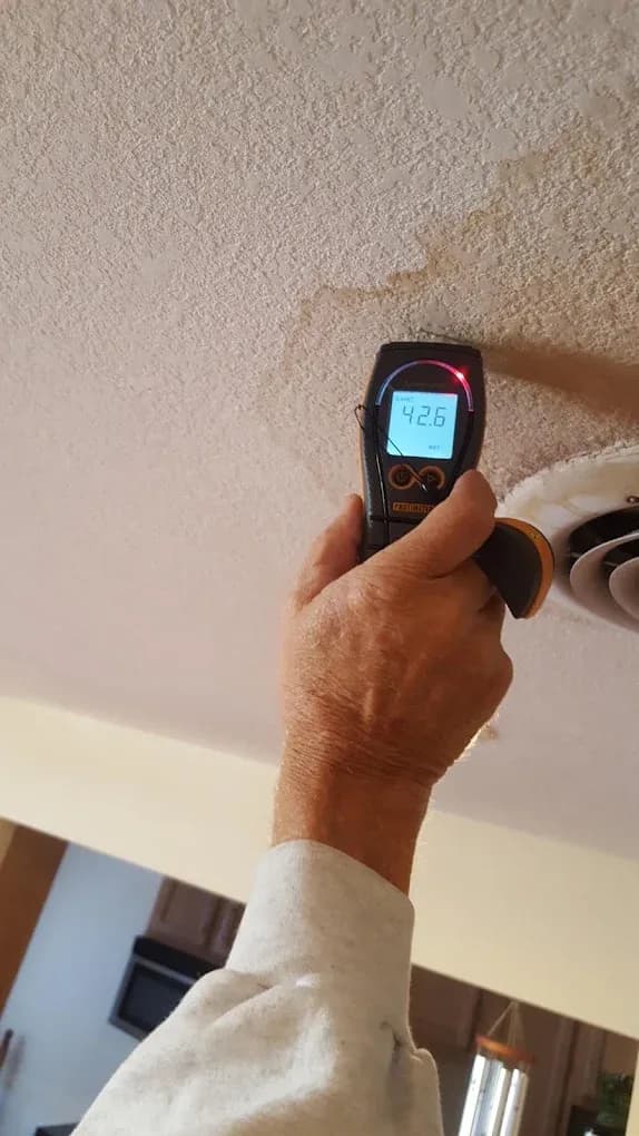 A moisture meter held against a water-stained ceiling, reading 42.6